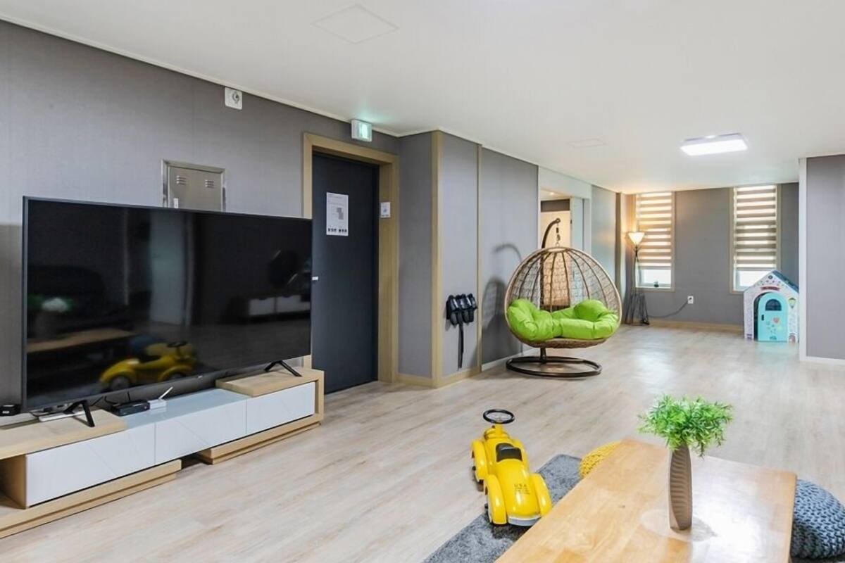 A modern living room with a flat-screen TV, a hanging chair, a small toy car, and a wooden coffee table.