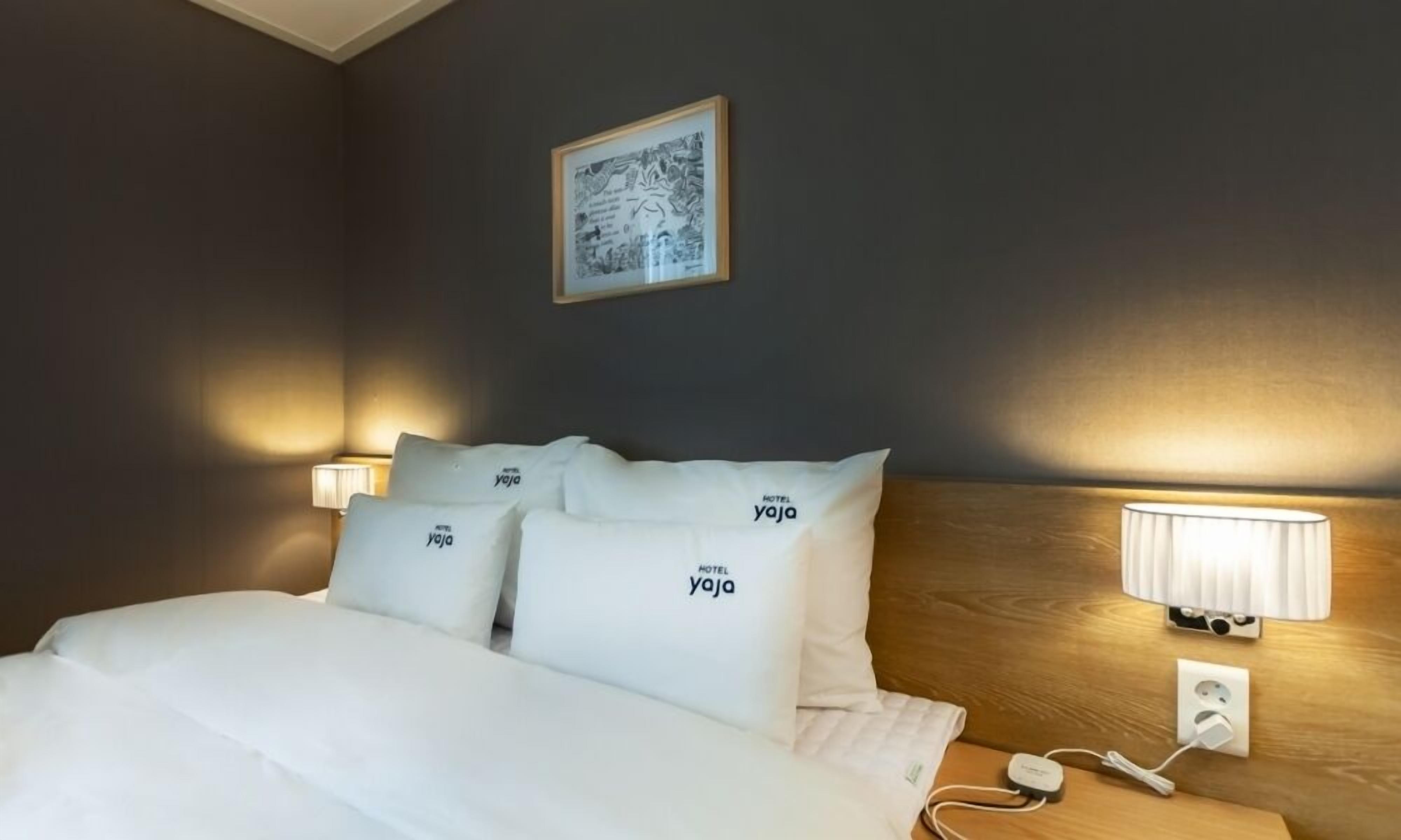 A hotel room with a bed, pillows, a bedside table, a lamp, and a wall-mounted picture.