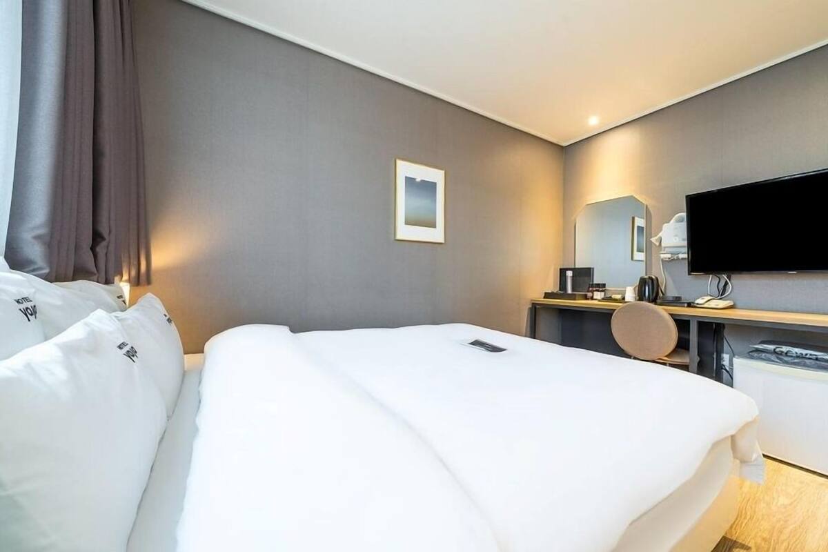 A hotel room with a bed, a desk, a chair, a television, and a mirror.