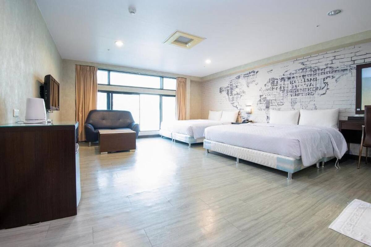 A hotel room with two beds, a desk, a chair, and a large window.