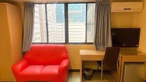 A room with a red chair, a desk, a television, and a window with curtains. - Newhotel (Kaohsiung)