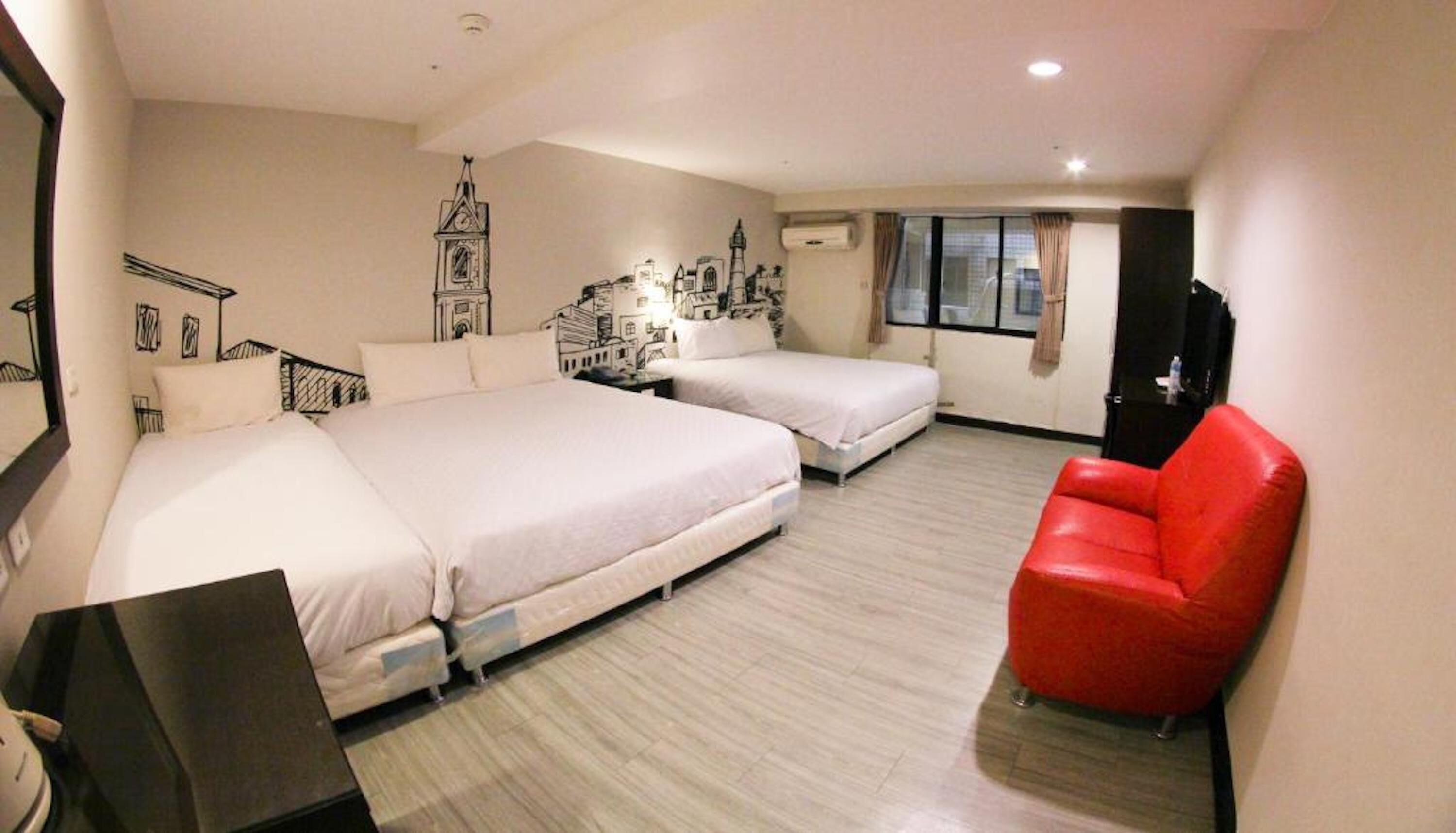 A hotel room with two beds, a red chair, and a cityscape mural on the wall.