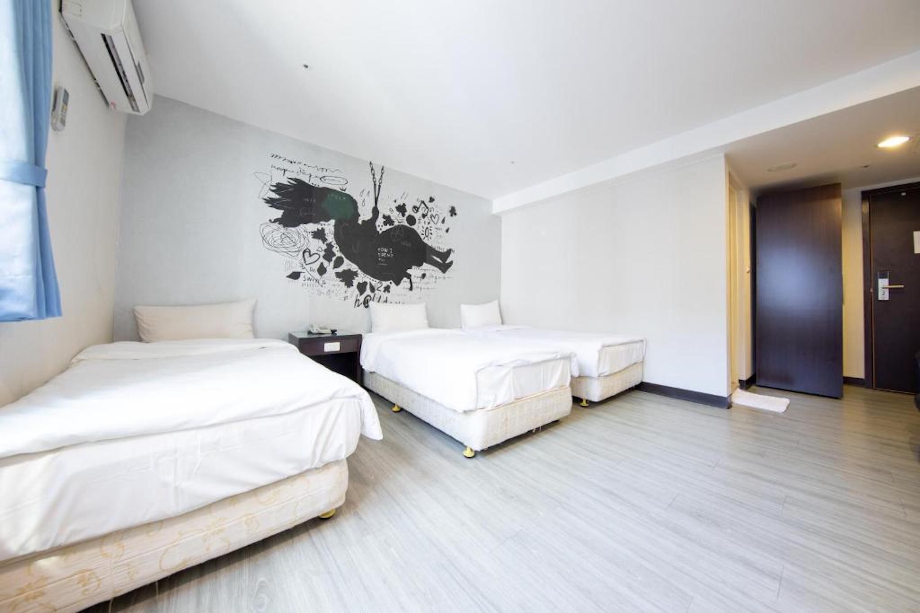 A hotel room with two single beds, a wall mural, and a wooden floor.