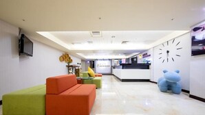 A modern hotel lobby with a reception desk, a large clock, and colorful seating areas. - Newhotel (Kaohsiung)