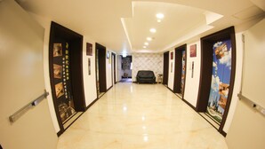 A hotel hallway with a shiny tiled floor, doors with posters, and a black chair in the center. - Newhotel (Kaohsiung)