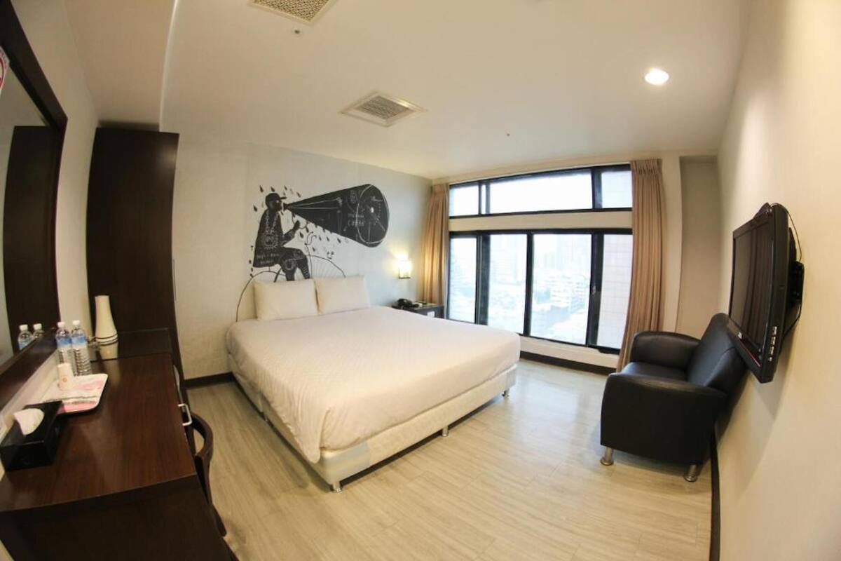 A hotel room with a large bed, a desk with a chair, a TV, and a window with curtains.