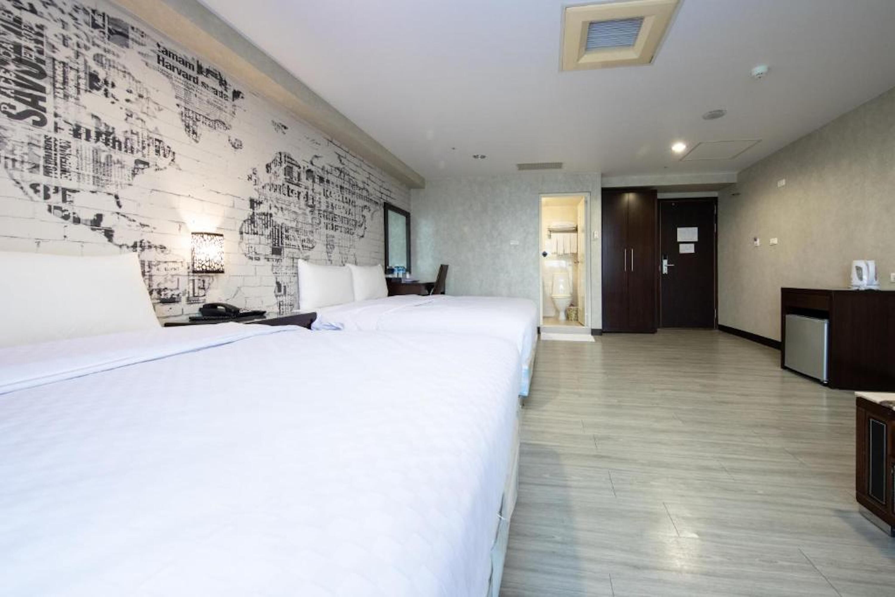 Quarto de hotel com uma cama grande, uma escrivaninha, uma cadeira e uma parede com um desenho de mapa.