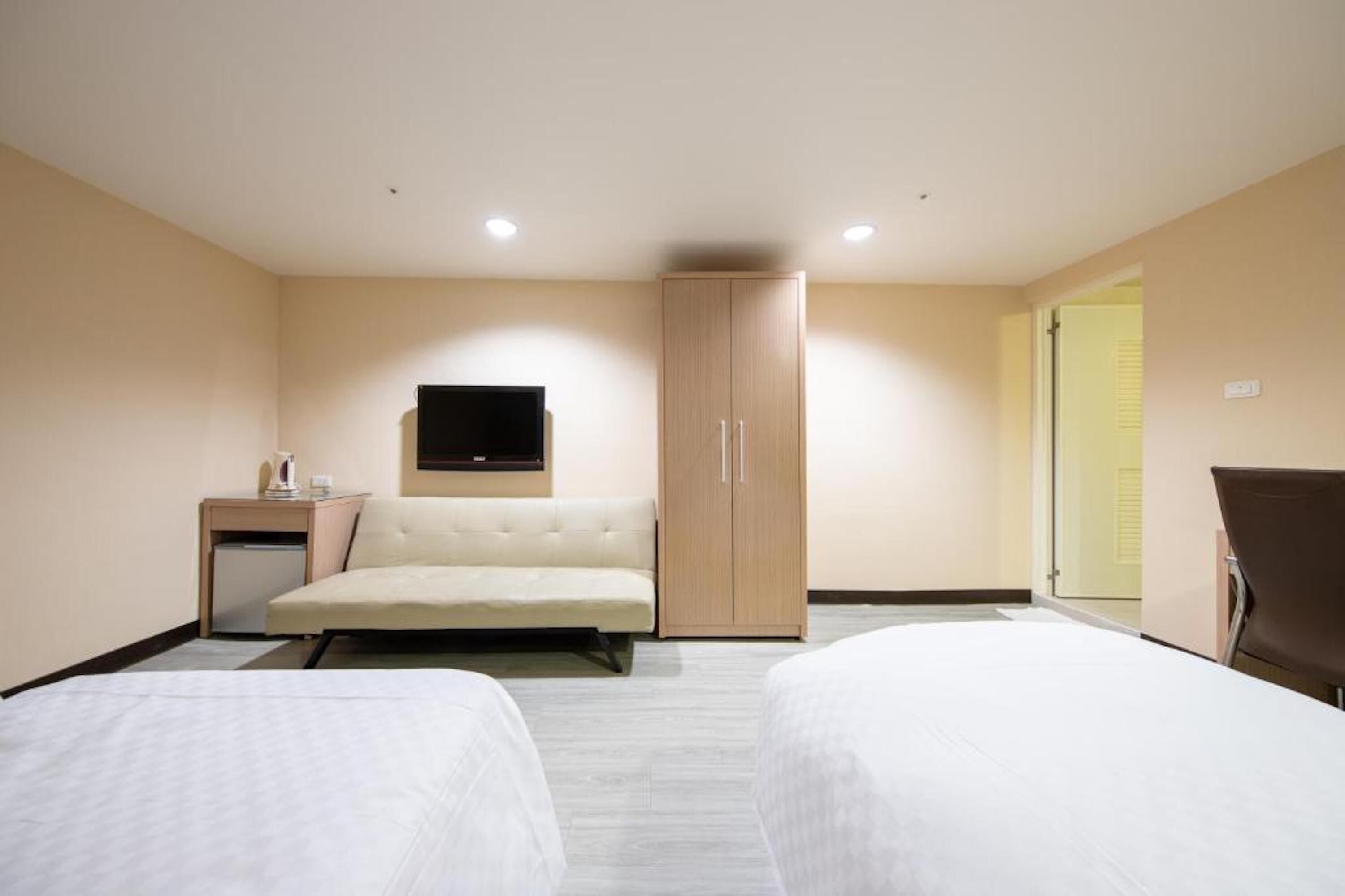Habitación de hotel con dos camas, un sofá, un televisor, un armario y un pequeño escritorio con lámpara.