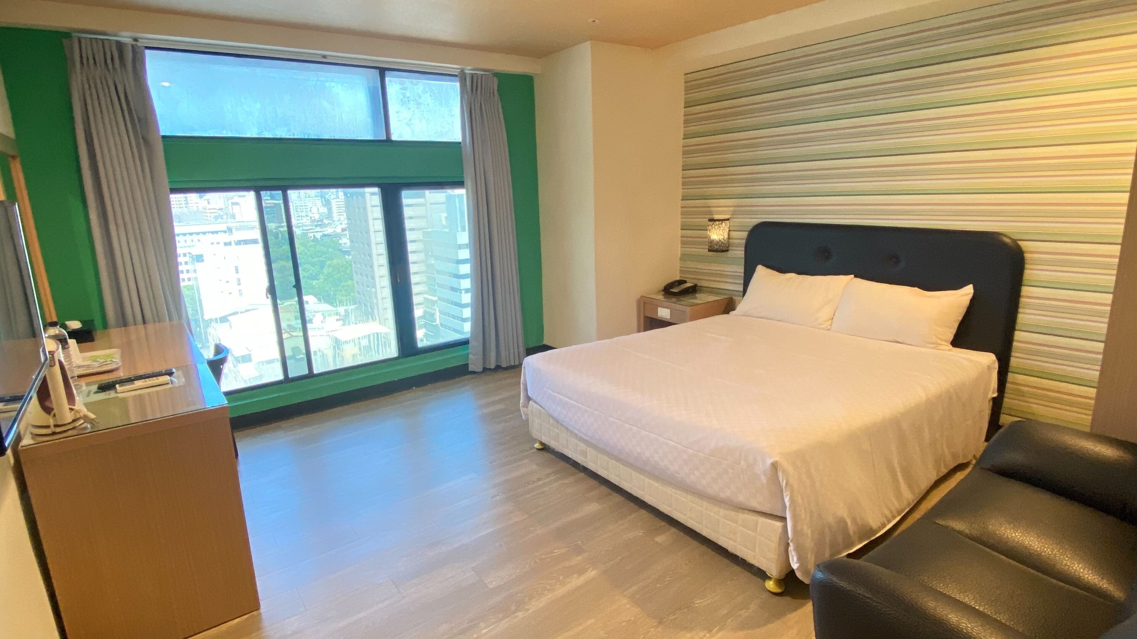 Una habitación de hotel con cama, escritorio y vistas a la ciudad a través de amplios ventanales.