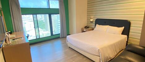 Una habitación de hotel con cama, escritorio y vistas a la ciudad a través de amplios ventanales.