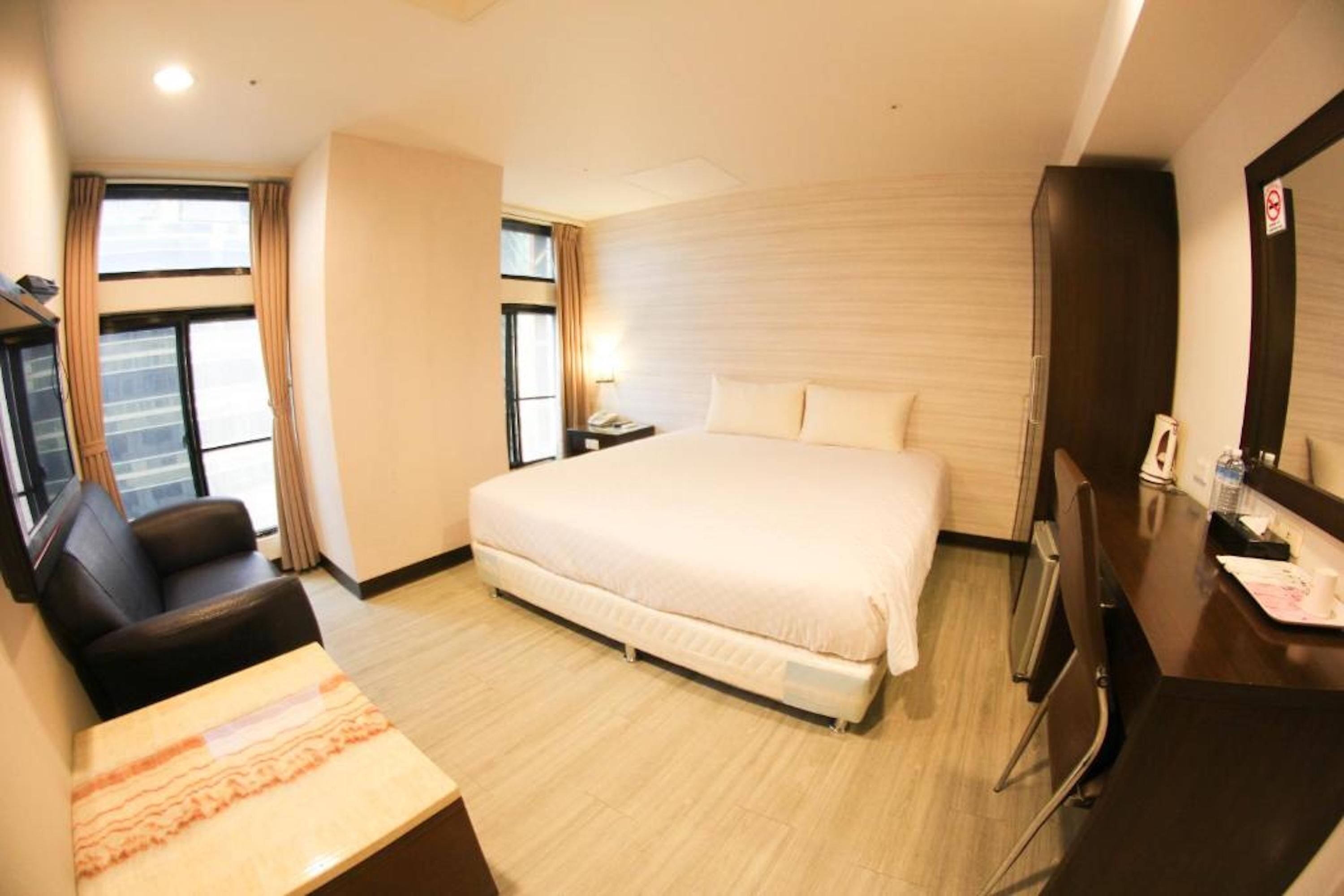 Habitación de hotel con una cama grande, un escritorio, una silla, un televisor y una ventana con cortinas.