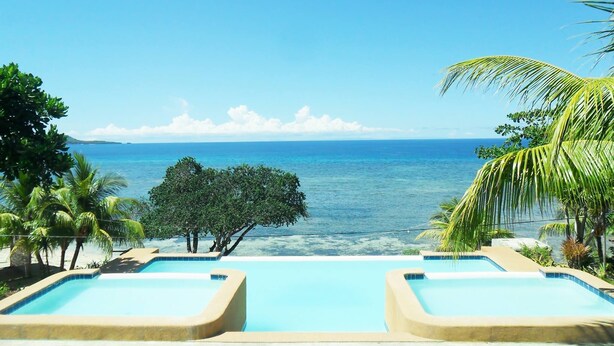 Zona piscina con acqua cristallina, circondata da palme e vista sull'oceano.