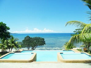 A pool area with clear blue water, surrounded by palm trees and a view of the ocean. - Maria Nico Mystic Island Resort (Maria)