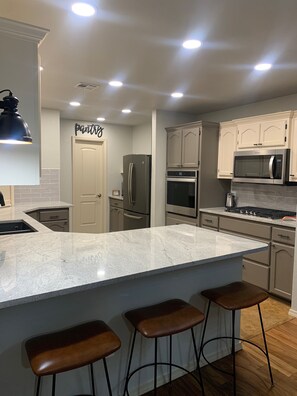 A modern kitchen with a large island, stainless steel appliances, and a 'pantry' sign on the wall. - City Comfort - Country Flair (Sand Springs)