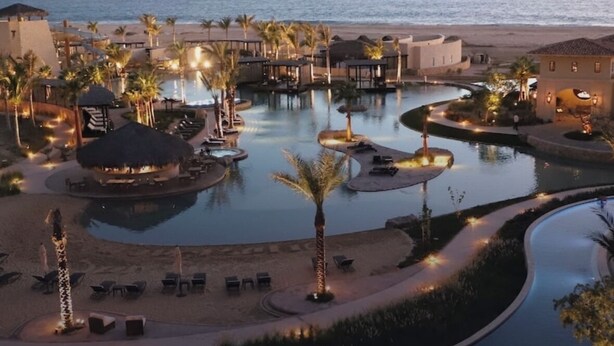 Un resort con piscina, palmeras y vista al mar.