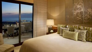 Habitación de hotel con una cama grande, una mesita de noche, una lámpara y vistas al océano a través de una puerta corrediza.