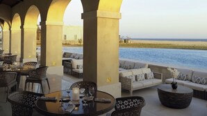 Un área de comedor al aire libre con mesas y sillas redondas, un sofá y vista al mar.