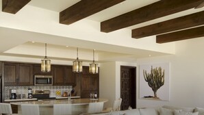 Una cocina moderna con armarios de madera, una isla central con taburetes de bar, iluminación colgante y un área de comedor con sofá y sillas.