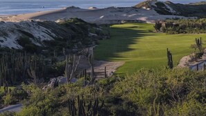 Un campo de golf con vista despejada al océano, dunas de arena y césped verde.