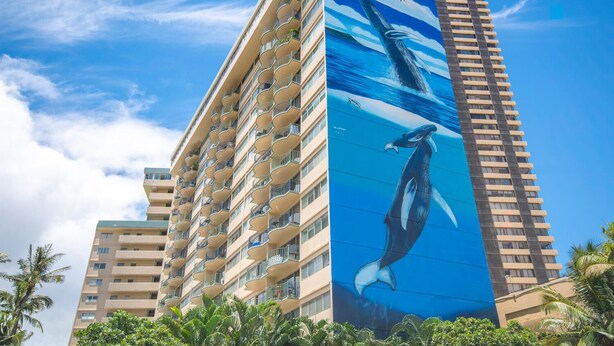Un hôtel de grande hauteur dont la façade est ornée d’une fresque remarquable représentant une baleine et un dauphin.