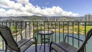 Un balcon avec deux chaises et une petite table, d’où l’on peut admirer une vue sur la ville, avec des montagnes en arrière-plan.