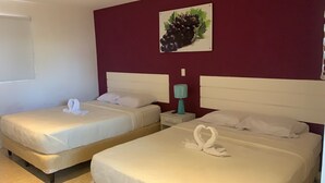 Dos camas individuales con ropa blanca, una mesita de noche color turquesa con una lámpara y un cuadro colgado en la pared de uvas.