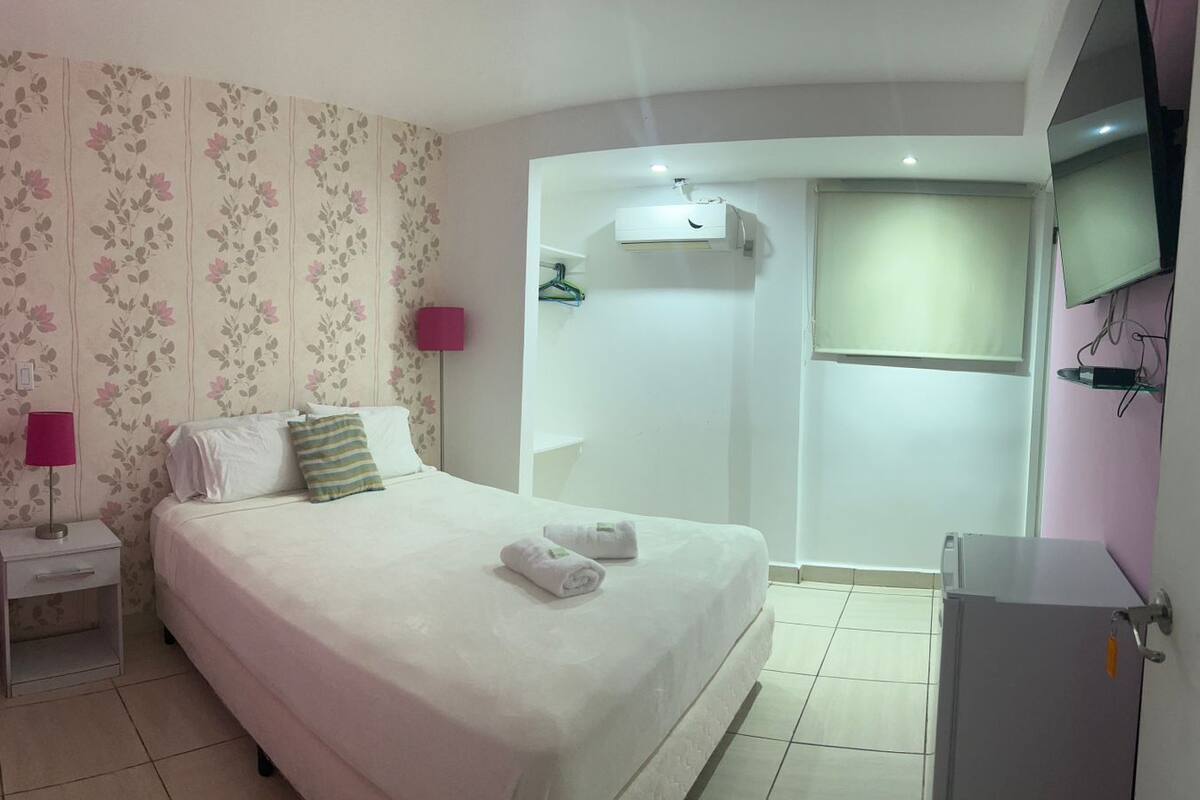 A bedroom with a bed, nightstand, lamp, and a wall-mounted TV.