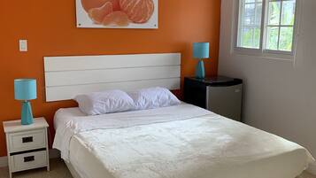 Ein Schlafzimmer mit einem weißen Bett, orangefarbenen Wänden, einem Fenster und einem Obstplakat.