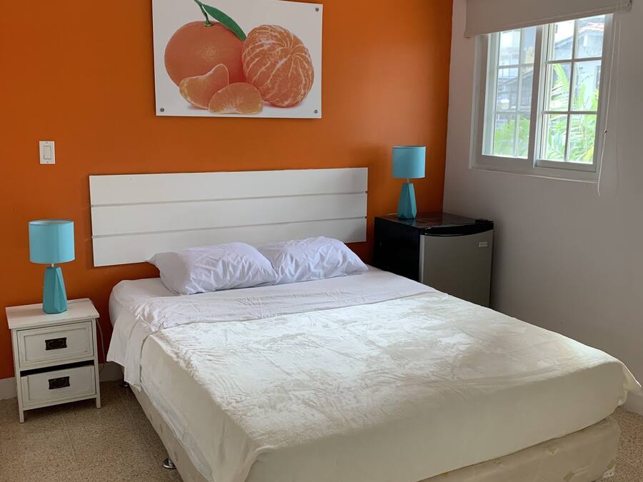 Ein Schlafzimmer mit einem weißen Bett, orangefarbenen Wänden, einem Fenster und einem Obstplakat.