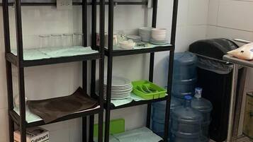 Een keuken met een zwarte metalen open kast vol keukengerei, een groene afdruiprek en grote watercontainers.