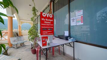 A hotel reception area with a sign advertising OYO My Budget Home Hotel & Apartment, a table with a bottle and a tissue box, and a view of the outdoors.