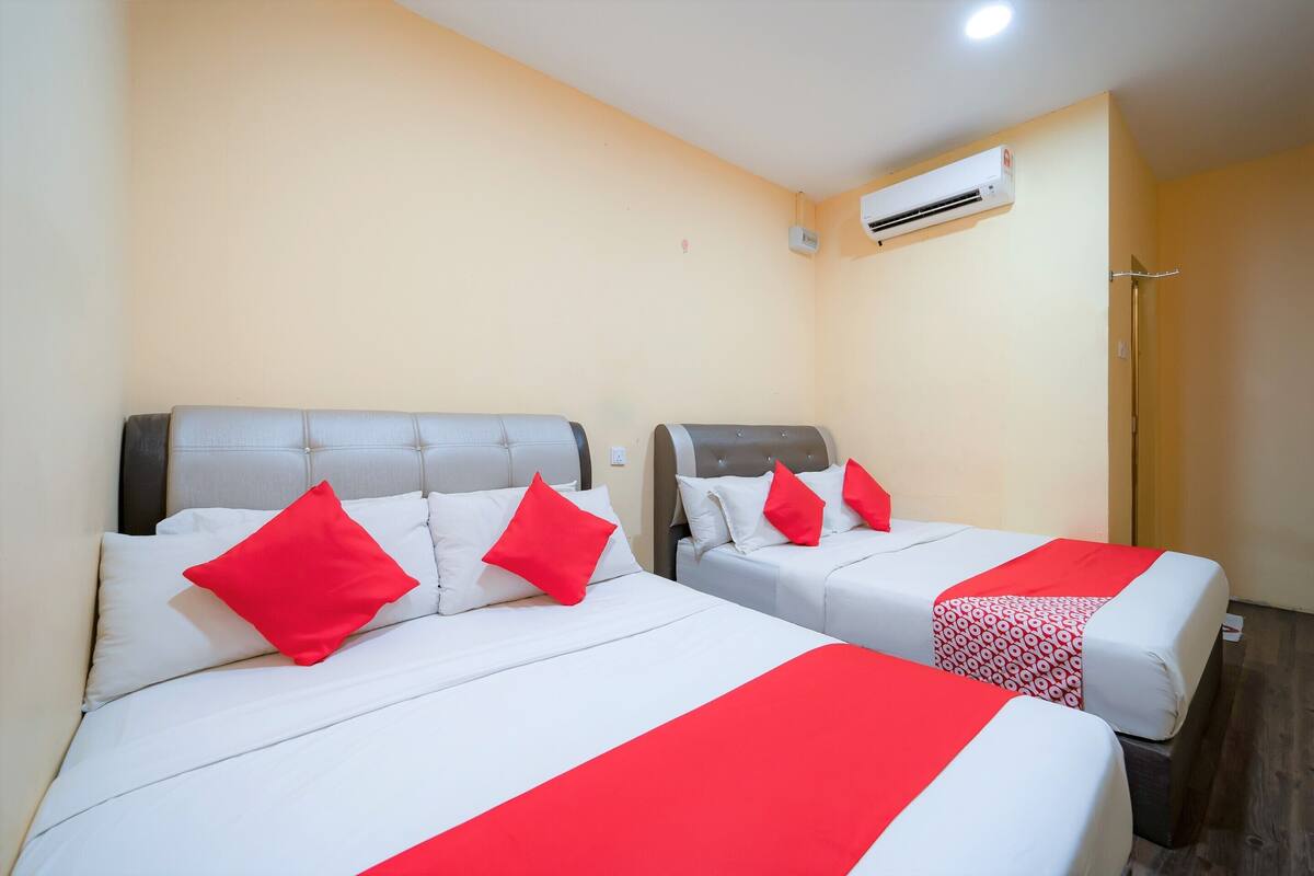 Two beds with red pillows and a red bedspread, an air conditioning unit on the wall, and a shower area.