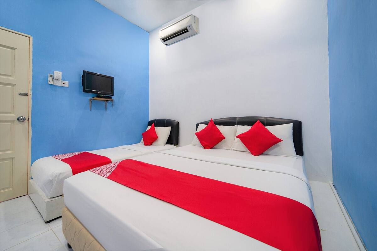 A hotel room with two beds, a TV, an air conditioner, and a door.
