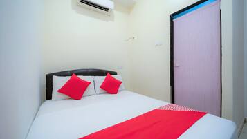 A bed with white bedding and red pillows, an air conditioning unit above it, and a door to the right.