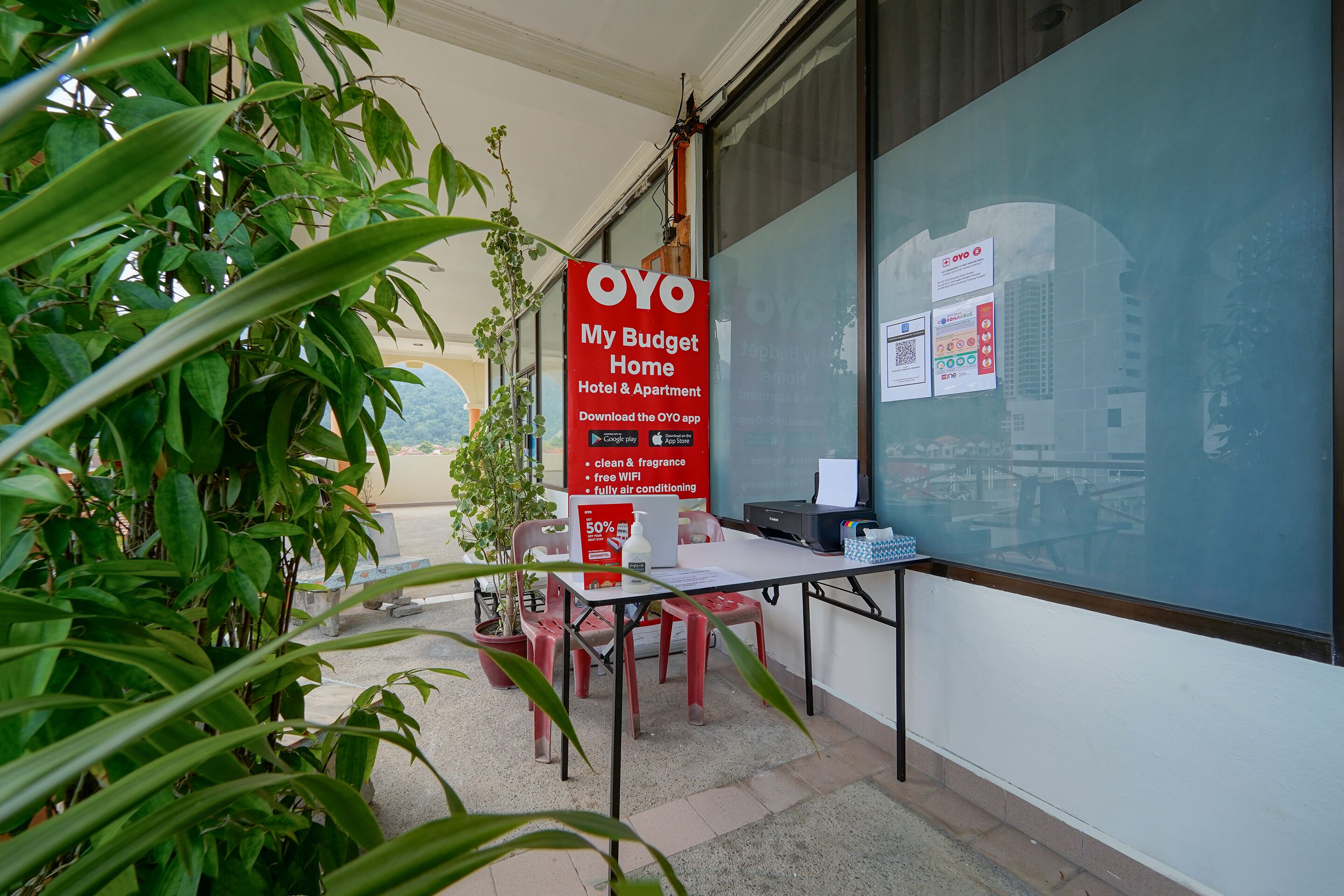 Esterno di un hotel con un cartello rosso che pubblicizza OYO My Budget Home, ambiente pulito e profumato, Wi-Fi gratuito e camere climatizzate.