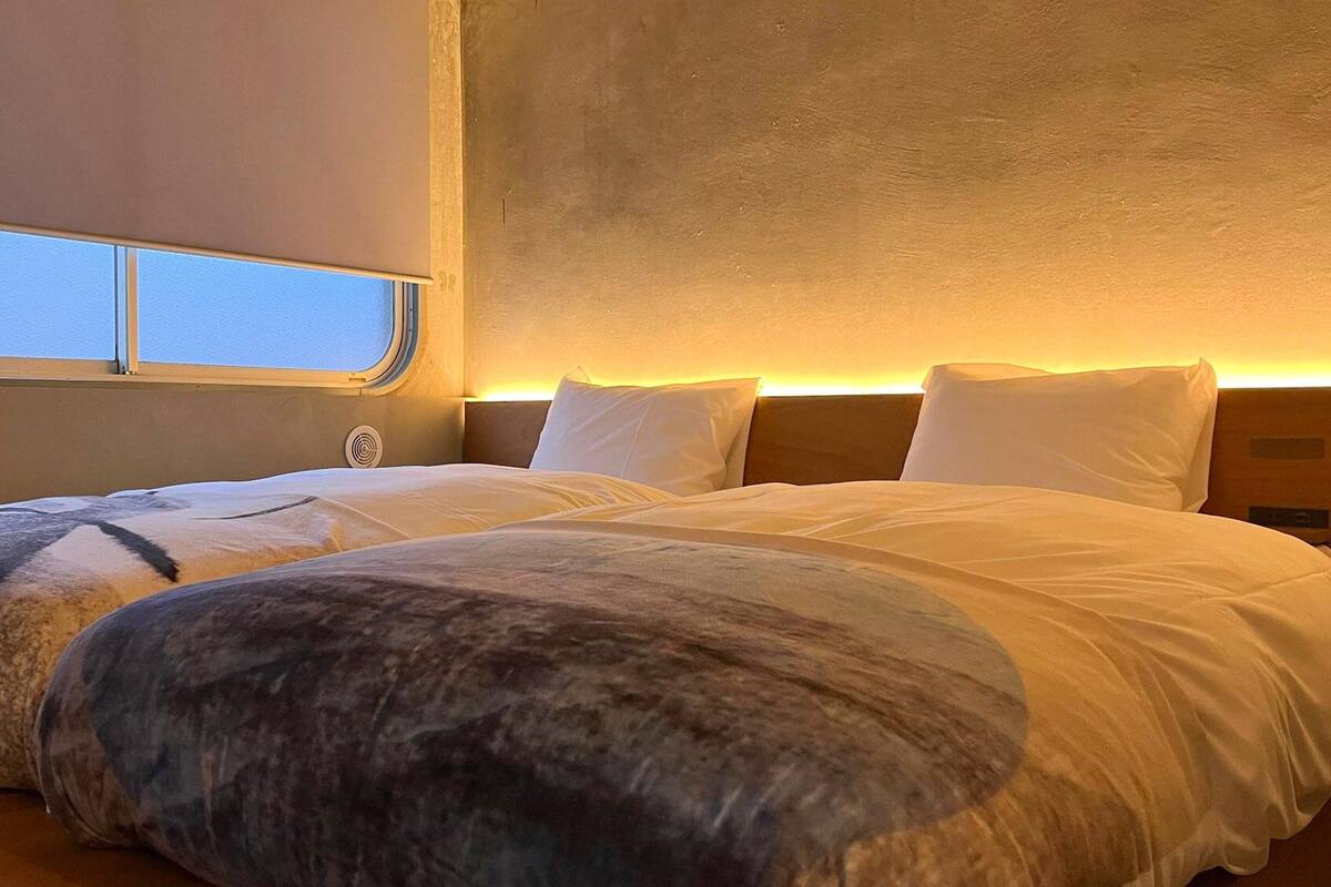 A double bed with a headboard, a window, and a wall-mounted air vent.