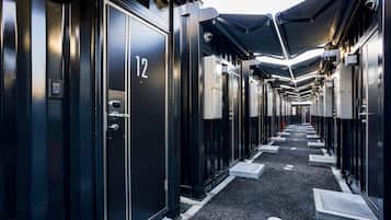 A corridor with numbered doors, a tiled floor, and overhead canopies.