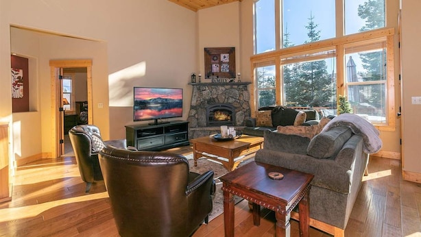 A spacious living room with a stone fireplace, leather furniture, and large windows offering a view of trees. - 5bd3ba, sleeps 10 Mountain View Hot Tub/Poker/Pool table, near Ski Resort (Truckee)