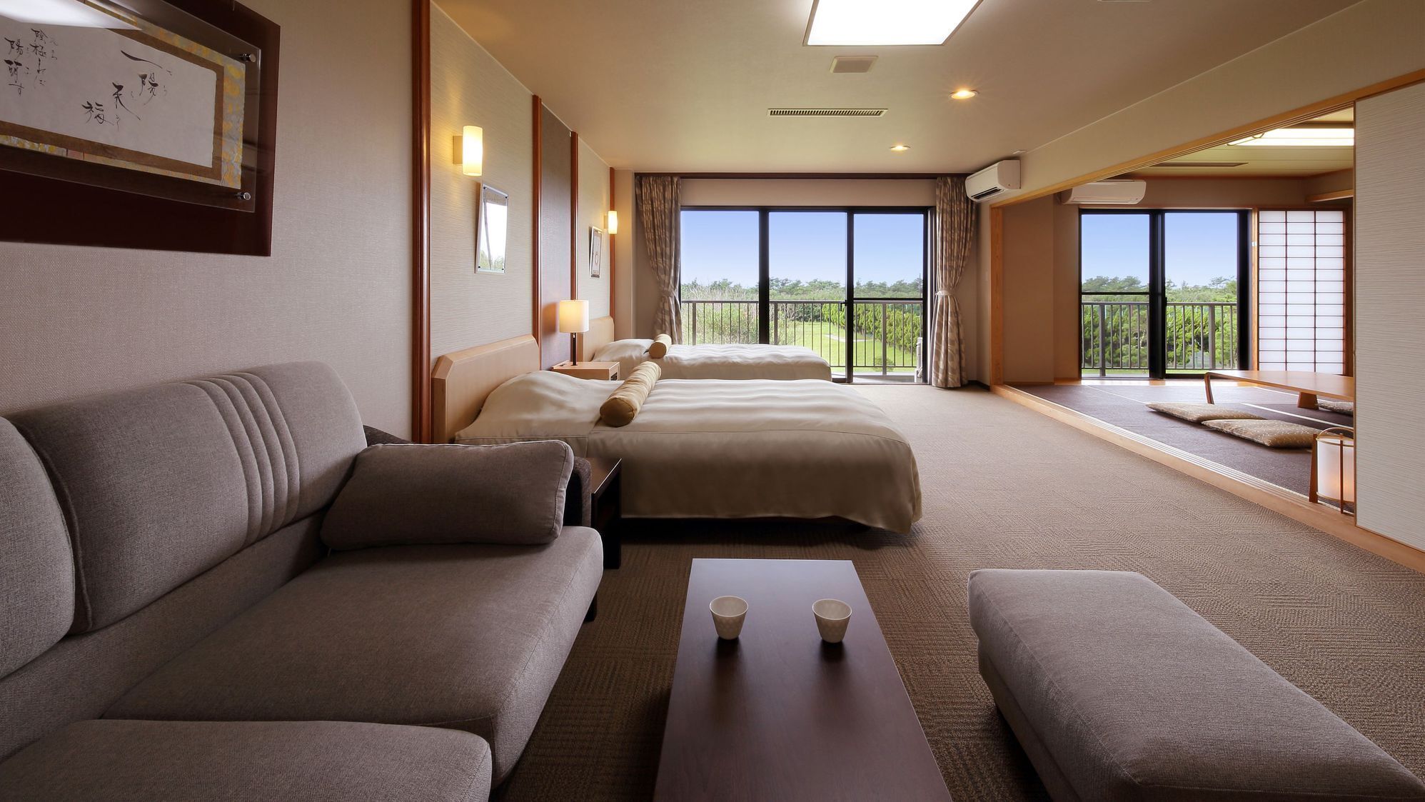 A hotel room with a sofa, two beds, a small table, and a view of the outdoors.