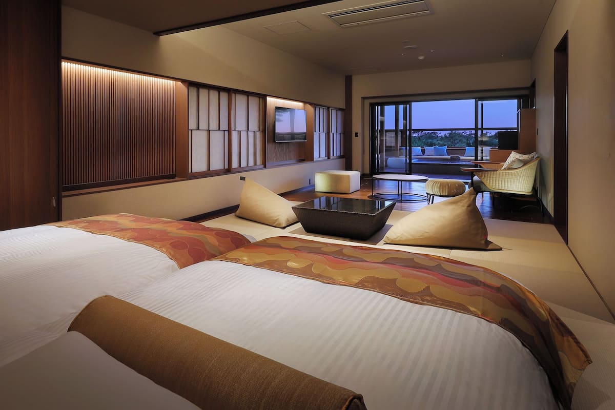A hotel room with a large bed, a small table, a chair, and a view of the outdoors.
