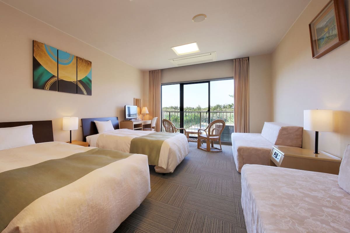 A hotel room with two beds, a desk, a chair, a TV, and a balcony with a view.