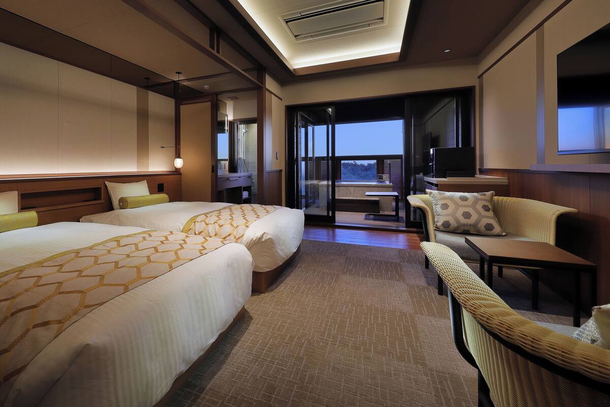 A hotel room with a large bed, a sofa, a small table, and a balcony with a view.
