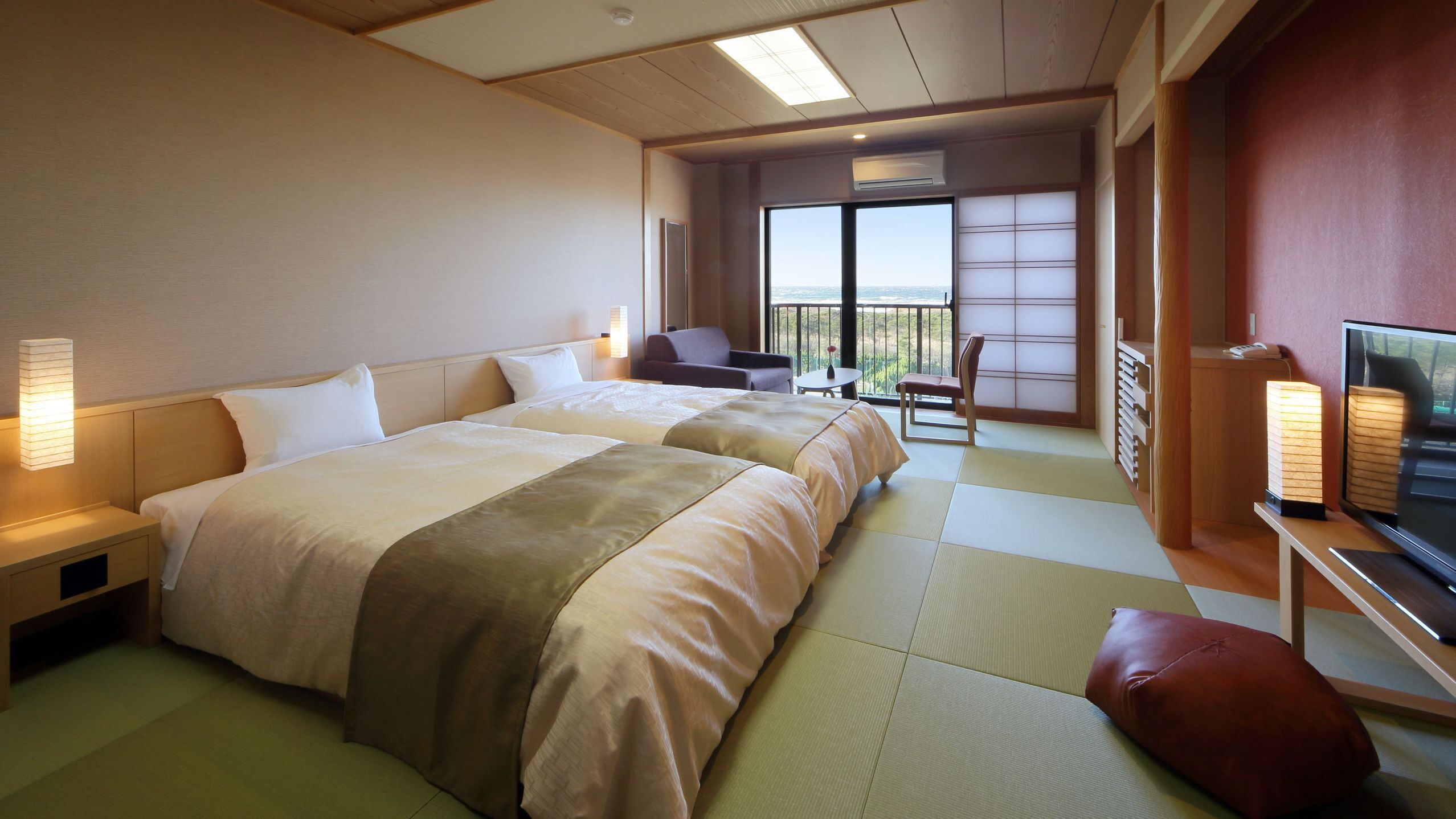 A hotel room with two beds, a TV, a balcony with a view, and a small table with chairs.