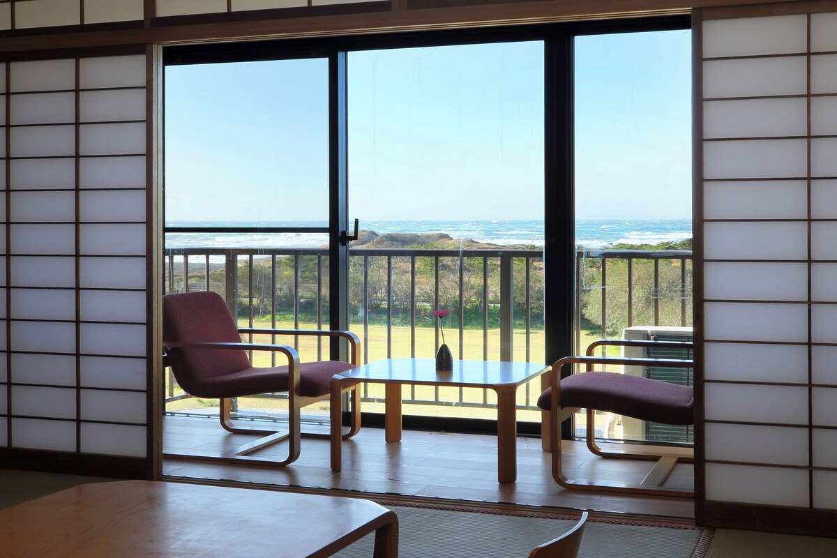 Ein Zimmer mit Meerblick, ausgestattet mit einer Schiebetür, zwei Stühlen und einem kleinen Tisch.