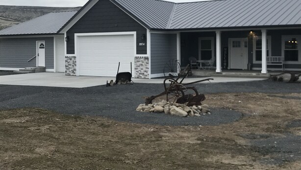 A two-story building with a garage, a porch with a bench, and a small garden area with rocks and a rake.