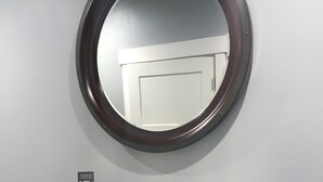 A dark wooden console with a round mirror above it, a small display case, and a door in the background.