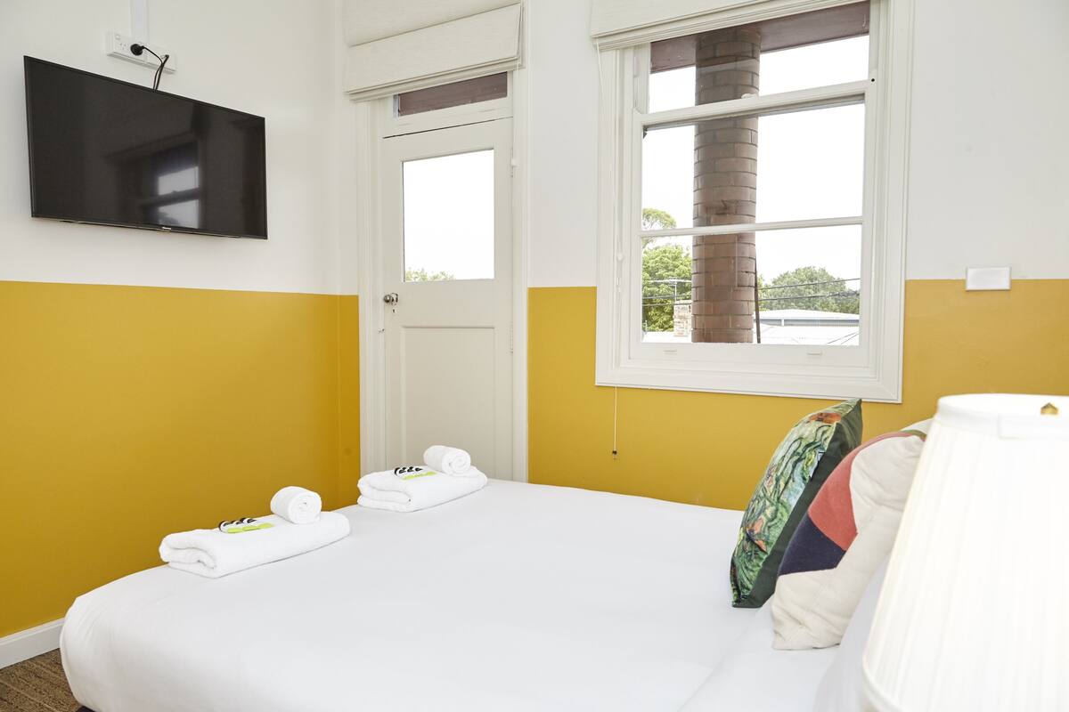 A hotel room with a bed, a TV mounted on the wall, a window with a view, and a door.
