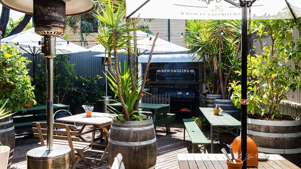 Un espace extérieur aménagé en terrasse, avec des tables et des bancs en bois, un barbecue et des plantes en pot.