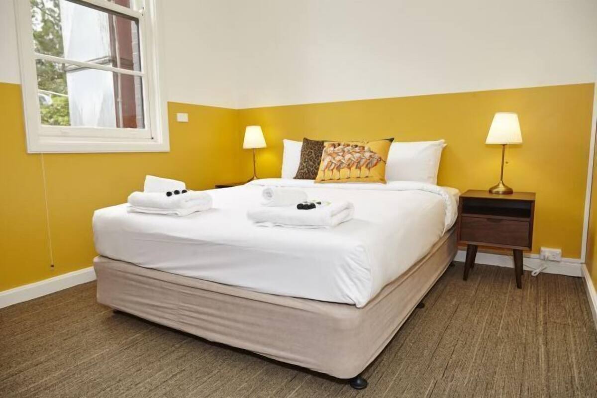 A hotel room with a bed, two bedside tables, a window, and a lamp.
