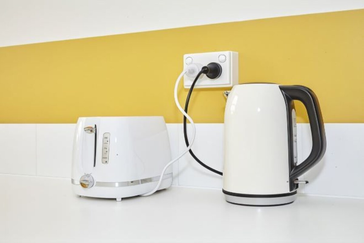 A white toaster and a white electric kettle on a white countertop with a yellow wall in the background.